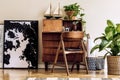 Stylish and vintage interior design of living room with wooden retro commode, chair, tropical plants, ships and elegant personal.