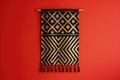 A stylish wall hanging with geometric patterns in black and gold, isolated on a solid ruby red background Royalty Free Stock Photo