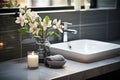 Stylish washbasin with a faucet against a background of dark tiles and flowers. Modern interior in Scandinavian style