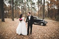 Stylish wedding couple, bride, groom kissing and hugging near retro car in autumn