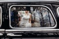 Stylish wedding couple sitting in beautiful black car, creative view from window. elegant groom and bride walking and holding Royalty Free Stock Photo