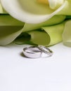 Stylish wedding rings made of white gold on a background of a bouquet of calla lilies