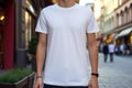 A stylish white blank t-shirt, worn by a model in an urban setting. Empty space for logo or design on the