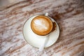 Stylish white cup of cappuccino with latte art on saucer and golden spoons on light wooden table.