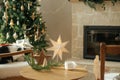 Stylish white cup, wooden star decor on table against stylish festive christmas tree with golden lights and cozy fireplace. Winter Royalty Free Stock Photo