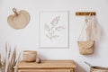 Stylish white interior of living room with mock up poster frame, rattan decoration, leaf, wooden shelf, dried flowers.