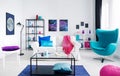 Stylish white living room with colorful accessories, white couch and metal coffee table in the middle next to blue egg chair, real