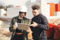 Stylish woman architect with tablet and contractor man checking blueprints at construction site. Young engineer or construction Royalty Free Stock Photo