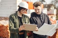 Stylish woman architect with tablet and contractor man checking blueprints at construction site. Young engineer or construction Royalty Free Stock Photo