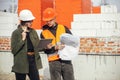 Stylish woman architect with tablet and contractor man checking blueprints at construction site. Young engineer or construction Royalty Free Stock Photo