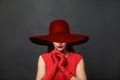 Stylish woman brunette with makeup and dark hair wearing red dress and red silk gloves and red wide broad brim hat on black Royalty Free Stock Photo