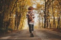 Stylish woman hipster in hat with backpack walking on road in sunny autumn woods. Young female traveler hiking in fall forest, Royalty Free Stock Photo