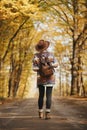 Stylish woman hipster in hat with backpack walking on road in sunny autumn woods. Young female traveler hiking in fall forest, Royalty Free Stock Photo