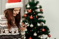 Stylish woman holding phone looking at screen at christmas tree Royalty Free Stock Photo