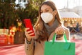 Stylish woman with KN95 FFP2 face mask watching her telephone holding shopping bags walking between Christmas Markets Royalty Free Stock Photo