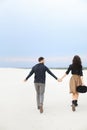 Stylish woman and man walking on snow and holding hands, wearing skirt and black shirt with hat, background. Royalty Free Stock Photo