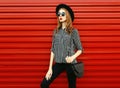 Stylish woman model wearing a black white striped shirt, round hat and handbag clutch on city street over red wall Royalty Free Stock Photo