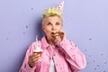 Stylish woman in party hat blowing noisemaker, celebrating birthday