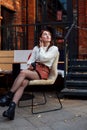 Stylish woman sitting on a cafe terrace with takeaway coffee and correcting her hairs while looking up