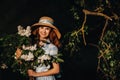 A stylish woman in a straw hat and a straw bag poses with a bouquet of white lilac in a Sunny spring Park. A quiet portrait of a