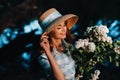 A stylish woman in a straw hat poses with a bouquet of lilacs, in a Sunny spring Park. A quiet portrait of a beautiful girl