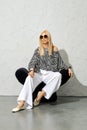 Stylish woman in striped blouse and wide trousers resting in modern chair under harsh light