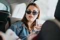 Stylish woman in sunglasses holding a bottle while sitting in a car