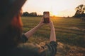 Stylish woman taking photo of sunset on phone in summer field. Atmospheric beautiful moment Royalty Free Stock Photo