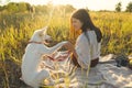 Stylish woman training her white dog on blanket in warm sunny light in summer meadow. Picnic