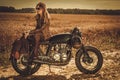 Stylish woman on the vintage custom cafe racer in a field. Royalty Free Stock Photo