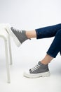 Stylish women`s grey sneakers on legs of model on chair on white background