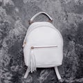 Stylish women\'s white leather backpack with a handle and zipped compartment with tassel pull isolated on a marble effect Royalty Free Stock Photo