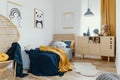 Stylish wooden commode in bright bedroom interior with poster on the wall