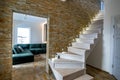 Stylish wooden contemporary staircase inside loft house interior. Modern hallway with decorative limestone brick walls and white Royalty Free Stock Photo