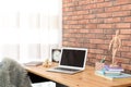 Stylish workplace interior with laptop on table near brick wall