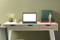 Stylish workplace with laptop, cup and vase of dry decorative spikes on white desk near olive wall indoors Royalty Free Stock Photo