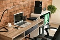 Stylish workplace with laptop on table near brick wall in office