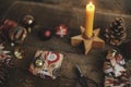 Stylish wrapped Christmas gift box, scissors, candle, red paper stars, golden ornaments on rustic wooden table. Atmospheric image Royalty Free Stock Photo