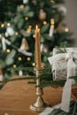 Stylish wrapped christmas gift, rustic basket with fir branches, candle and modern decorations against festive decorated tree in Royalty Free Stock Photo