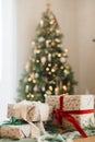 Stylish wrapped christmas gifts with ribbon on table on background of decorated christmas tree, rustic fireplace and festive