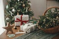 Stylish wrapped christmas gifts, rustic basket with fir branches and modern decorations against festive decorated tree in Royalty Free Stock Photo