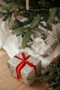 Stylish wrapped christmas gifts and rustic basket with fir branches under festive decorated christmas tree in scandinavian room. Royalty Free Stock Photo