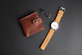 Stylish wrist watch, cuff links and wallet on black background.