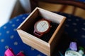 Stylish wristwatch in a wooden box. In background Pink bow tie, beautiful glass cufflinks, flower boutonniere. A men's set of acc Royalty Free Stock Photo