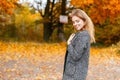 Stylish young beautiful woman with a cute smile in a gray vintage coat posing in autumn park with yellow-orange foliage. Royalty Free Stock Photo