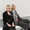 Stylish young beautiful women with blond hair in fashion jackets outdoors. Two fine fashionable girlfriends in vintage clothes in