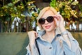 Stylish young blonde in sunglasses sitting at a table in a beautiful restaurant waiting for an order. The woman has a break in the Royalty Free Stock Photo