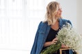 Stylish young blonde woman with a bouquet of gypsophila. Portrait in the interior.