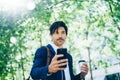 Stylish young businessman using smartphone for listining music while walking in city park and holding take away coffee Royalty Free Stock Photo