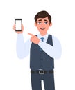 Stylish young businessman in vest suit showing blank mobile, cell phone and pointing finger. Trendy person holding smartphone.